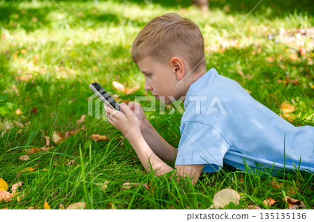 teenage boy engrossed in phone lying on green grass 135135136