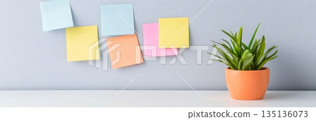Colorful sticky notes on a wall represent the chaos of multitasking and time management. A green plant in an orange pot adds a touch of calm to the organized workspace 135136073