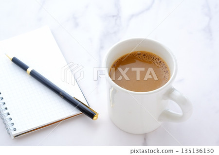 An image of working at a desk with a ring-type notepad and pen while drinking coffee. 135136130