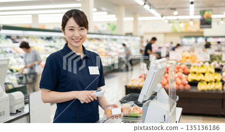 一位三十多歲的日本女店員身穿制服，微笑著在一家大型超市的收銀台為顧客服務。 135136186