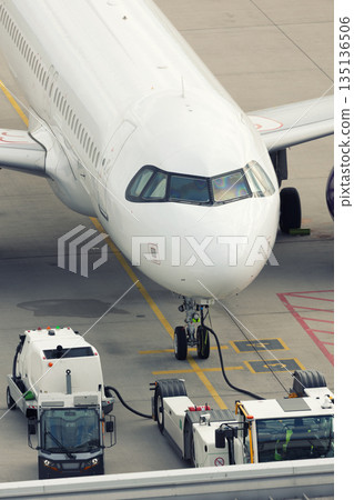 Modern regional  jet aircraft airport tarmac connected to ground vehicles for refueling maintenance. Engine cockpit clearly visible crew performs technical operations before next scheduled flight 135136506