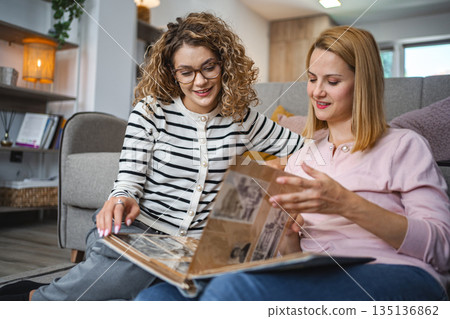Two female friends looking at an old photo album at home 135136862
