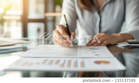 Businesswoman examining financial charts and graphs, taking notes during an office meeting, demonstrating professionalism and expertise in financial analysis 135137195