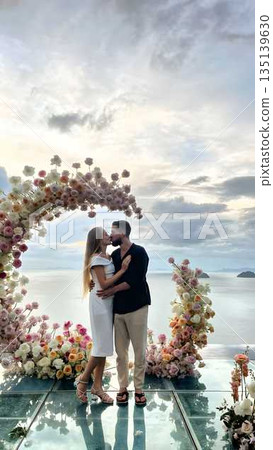 Romantic couple kissing under floral wedding arch by the sea 135139630