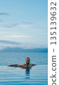 Relaxed man enjoying infinity pool with ocean view during tropical vacation 135139632