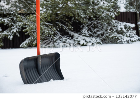 Snow shovel standing upright in fresh white snow outdoors. Winter home maintenance concept with copy space, cold weather and seasonal snowfall background. 135142077