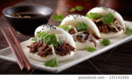 Close-up of three mouthwatering steamed buns filled with savory braised meat, garnished with fresh cilantro and sesame seeds, arranged on a white rectangular plate. 135142490