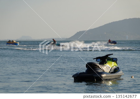 Water transport at sea.Two jet skis carrying tourists glide across the sea. One jet ski awaits tourists. Water transport at sea.Two jet skis carrying tourists glide across the sea. One jet ski awaits tourists. 135142677