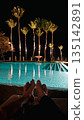 Couple relaxing by luxury pool at night with palm trees. 135142891