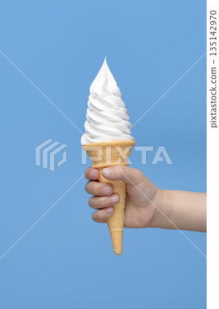 手中拿著香草軟冰淇淋甜筒，背景是藍色背景 135142970