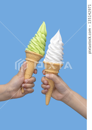 夏日甜點：兩隻手分別拿著抹茶和香草口味的軟冰淇淋甜筒，背景是藍色。 135142971