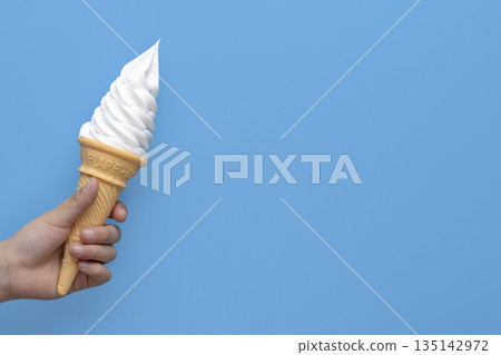 手中拿著香草軟冰淇淋甜筒，背景是藍色的，留有文字空間。 135142972