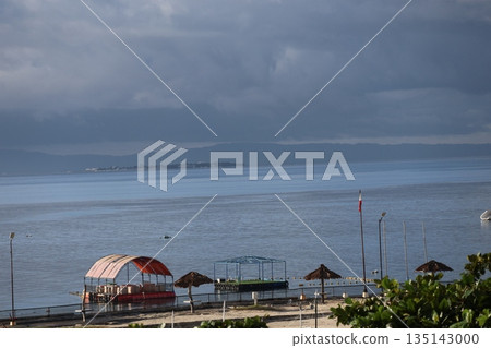 A view of Cebu Island with the resort coastline, blue ocean, islands, mountains on the opposite shore, and a cloudy sky A view of Cebu Island with the resort coastline, blue ocean, islands, mountains on the opposite shore, and a cloudy sky 135143000