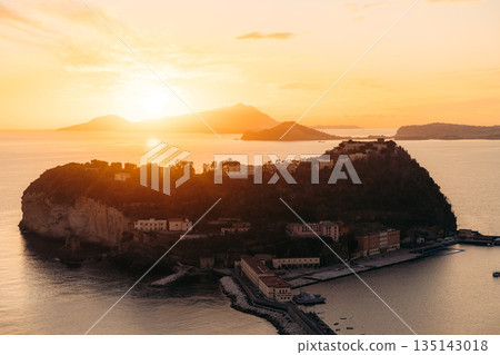 Sunset over Nisida with buildings on a hill and mountains in the distance. Naples, Italy Sunset over Nisida with buildings on a hill and mountains in the distance. Naples, Italy 135143018