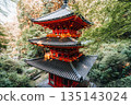 A vibrant red Japanese pagoda stands amidst lush green trees 135143024