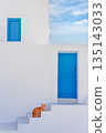 Ginger cat relaxing on white steps outside a traditional Greek island house 135143033