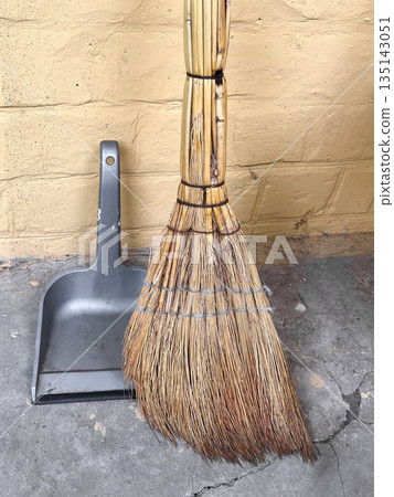 A broom and dustpan set against a yellow brick wall. A broom and dustpan set against a yellow brick wall. 135143051
