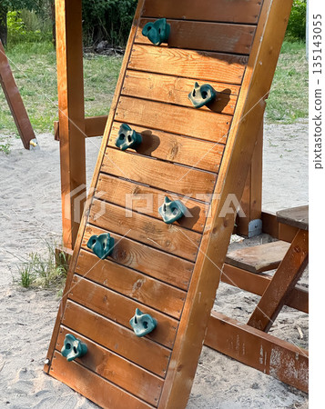 Wooden climbing wall on playground with sand and greenery. Wooden climbing wall on playground with sand and greenery. 135143055