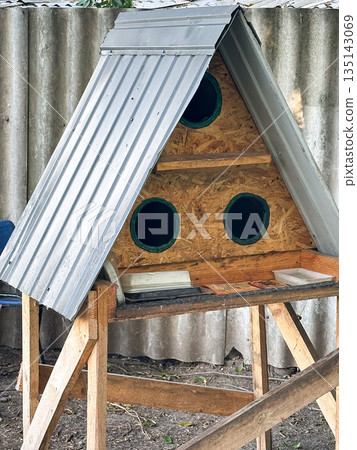 Triangular birdhouse with metal roof in a garden setting. Triangular birdhouse with metal roof in a garden setting. 135143069