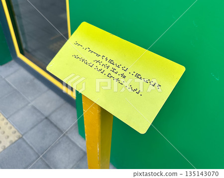 Yellow braille sign on a pole outside a building entrance. Yellow braille sign on a pole outside a building entrance. 135143070