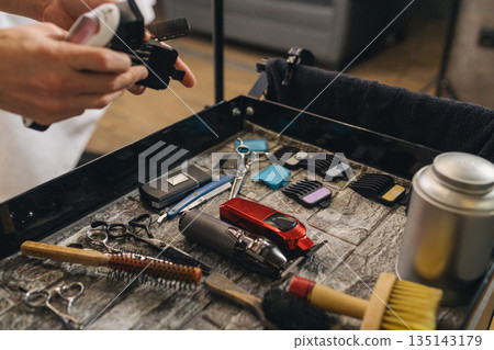 Barber workstation with professional grooming tools and electric clippers. Close up of hairstyling equipment on salon trolley, preparation for haircut, modern barbershop interior. 135143179