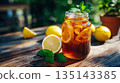 Refreshing drink in a glass jar with lemon and mint, perfect for a sunny day. The iced beverage glistens on a wooden table, inviting relaxation and enjoyment. 135143385