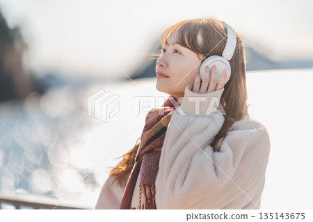 一位年輕女子站在海邊,戴著耳機聽音樂。 一位年輕女子站在海邊,戴著耳機聽音樂。 135143675