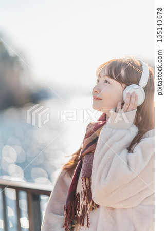 一位年輕女子站在海邊,戴著耳機聽音樂。 一位年輕女子站在海邊,戴著耳機聽音樂。 135143678