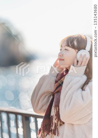 Young woman standing by the seaside listening to music with headphones Young woman standing by the seaside listening to music with headphones 135143680