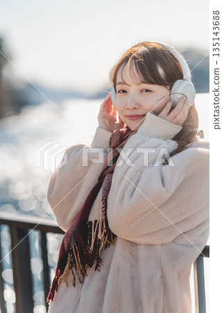 一位年輕女子站在海邊，戴著耳機聽音樂。 135143688