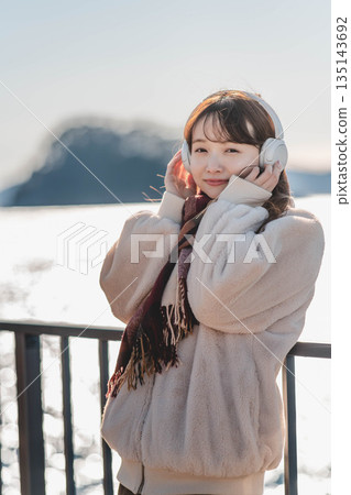 一位年輕女子站在海邊,戴著耳機聽音樂。 一位年輕女子站在海邊,戴著耳機聽音樂。 135143692