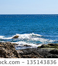 A Tranquil Coastal Scene Featuring Gentle Waves Crashing Against Rugged Rocks Under a Clear Blue Sky, Illustrating Nature's Beauty and Serenity 135143836