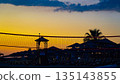 Beach Volleyball at Sunset: A Serene Scene with Silhouettes of Lounge Chairs, Palms, and a Colorful Sky Perfect for Relaxation and Recreation 135143855