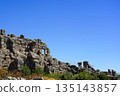 Ancient Stone Ruins Under a Clear Blue Sky Highlighting the Remnants of a Historic Civilization Surrounded by Greenery and Natural Beauty 135143857