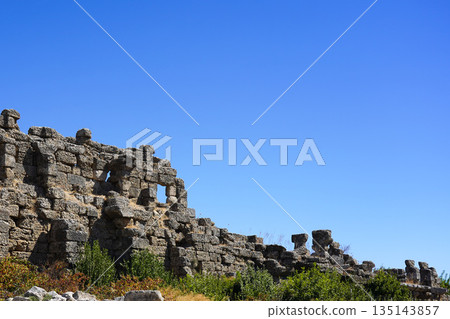 Ancient Stone Ruins Under a Clear Blue Sky Highlighting the Remnants of a Historic Civilization Surrounded by Greenery and Natural Beauty 135143857