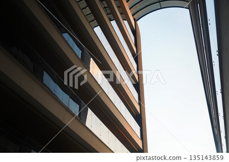 A Dramatic View of Modern Architectural Design Showcasing Sleek Lines and Glass Features Against a Clear Sky 135143859