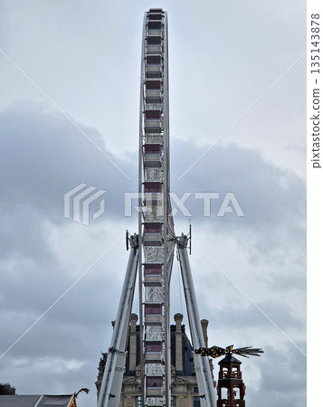 Grande Roue de Paris Ferris Wheel at the Tuileries Christmas market. The massive, modern ride contrasts with the historic architecture on the Louvre in background and nearby festive fair 135143878
