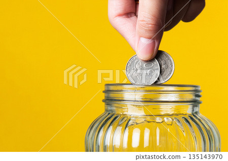 Hand dropping coins into glass jar for savings 135143970