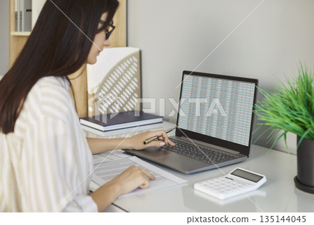 Young business woman accountant working on laptop computer with tables at office. Young business woman accountant working on laptop computer with tables at office. 135144045