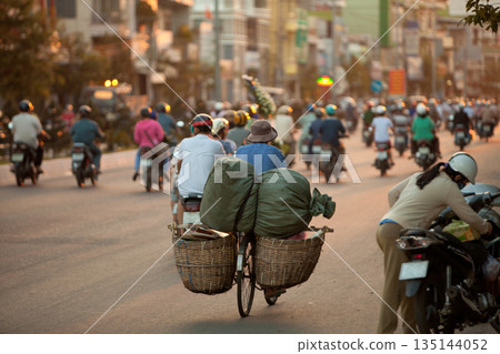 Evening rush hour with motorcycle riders in Asian city, soft focus on bicycle with two baskets. 135144052