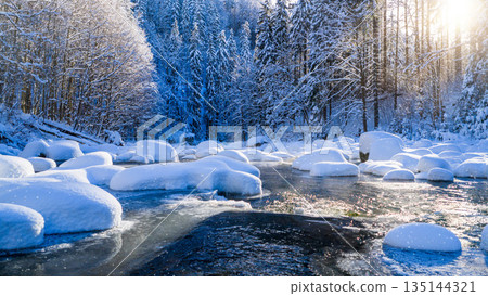 Peaceful winter river flowing through a snow covered forest during gentle snowfall. Soft sunlight reflects on icy water, creating a calm, atmospheric, and serene winter nature scene. Peaceful winter river flowing through a snow covered forest during gentle snowfall. Soft sunlight reflects on icy water, creating a calm, atmospheric, and serene winter nature scene. 135144321