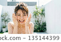 A woman washing her face outdoors with water and showing a big smile 16:9 135144399