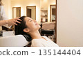 A smiling Japanese woman relaxing after receiving a head spa at the shampoo station in a beauty salon 135144404