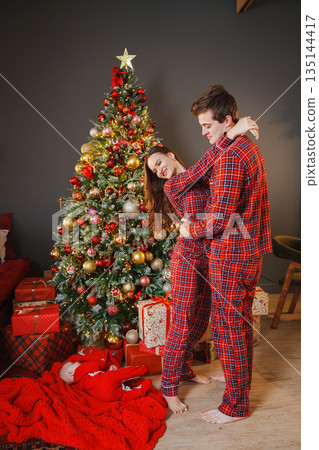 Couple in pajamas near Christmas tree with presents Couple in pajamas near Christmas tree with presents 135144417