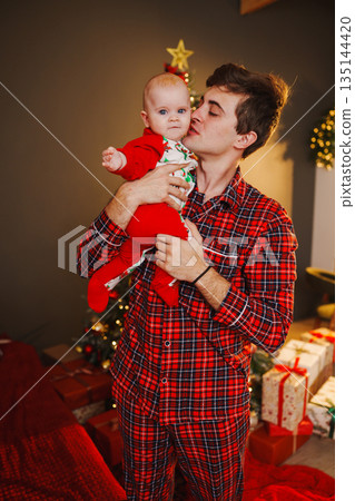 Father holds baby during Christmas celebration at home Father holds baby during Christmas celebration at home 135144420