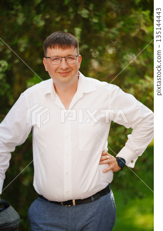 Smiling man in a white shirt poses outdoors on a sunny day Smiling man in a white shirt poses outdoors on a sunny day 135144443