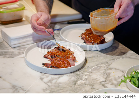 Chef preparing dishes with sauce at a modern kitchen 135144444