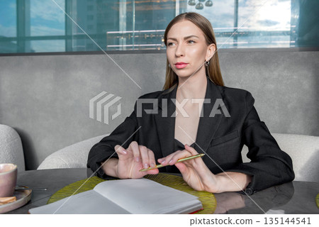 A girl sits at a table with a thoughtful face over a sketchpad. A girl sits at a table with a thoughtful face over a sketchpad. 135144541