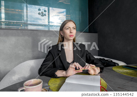 A girl sits at a table with a thoughtful face over a sketchpad. A girl sits at a table with a thoughtful face over a sketchpad. 135144542