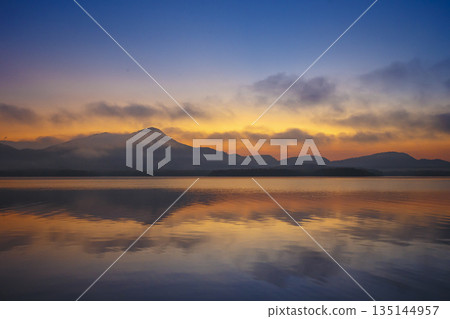 A cinematic sunset view featuring colorful skies, mountains, and calm water 135144957